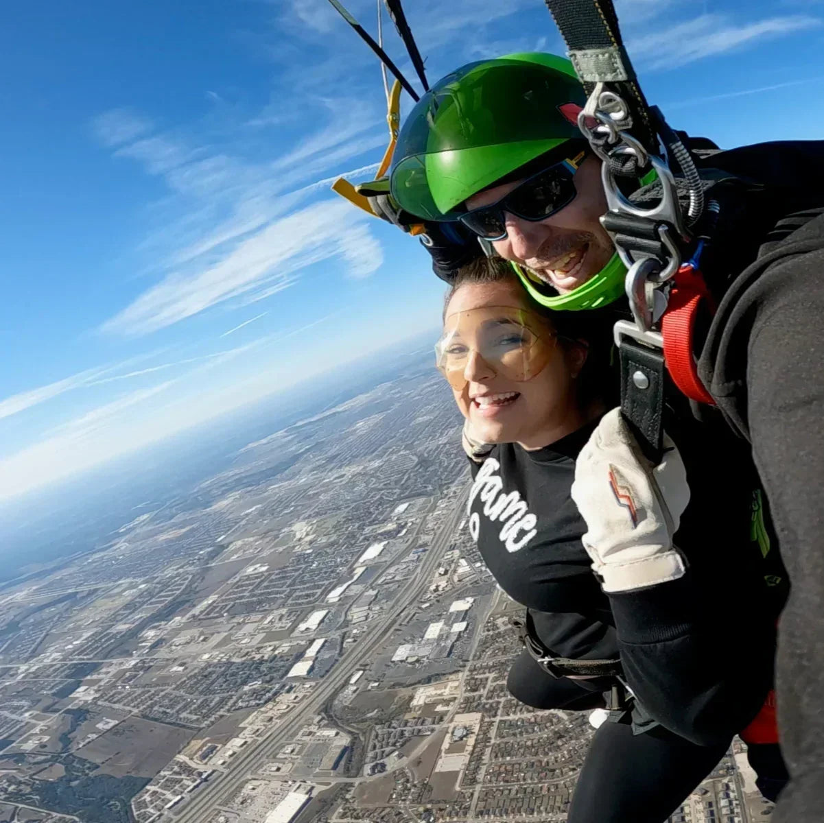 Two people smiling mid-air while steering a parachute during a tandem skydive