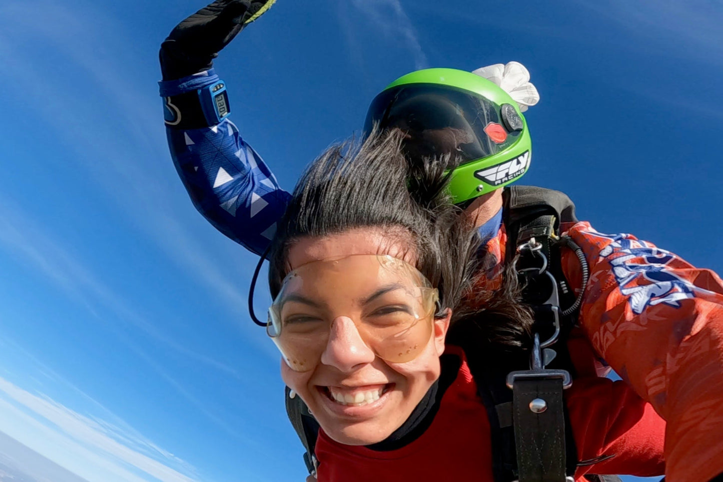 Happy skydiving passenger captured mid-air under a vibrant blue sky.