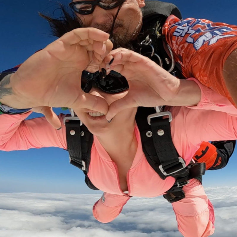 Skydiving duo creating heart hand signs mid-air, capturing a moment of fun and connection.