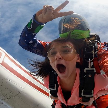 Tandem skydive exit shot featuring the instructor throwing a peace sign mid-air as they leap from the plane into the open sky