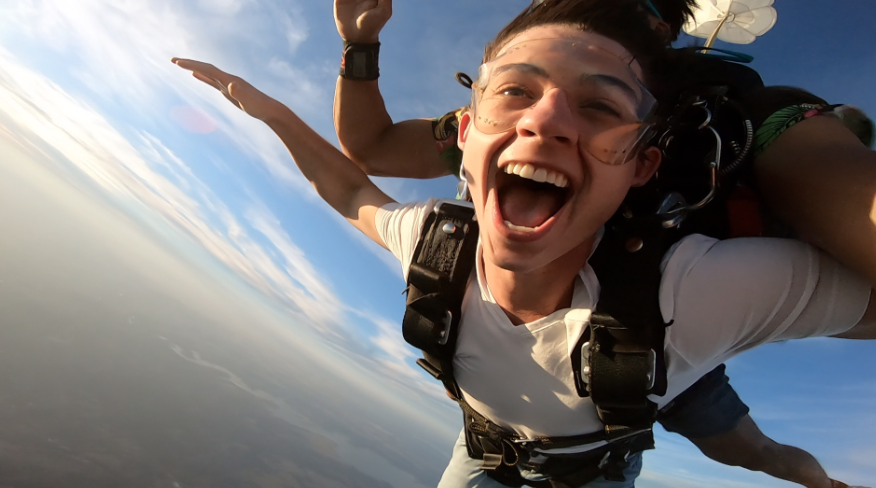 Selfie of a tandem skydiving passenger in freefall during a stunning sunset, capturing the excitement and golden hues of the sky.