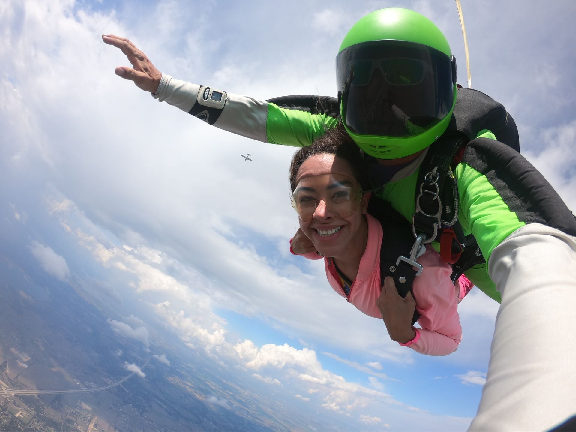 Tandem skydivers in freefall on a cloudy day, with the plane fading into the distance against a dramatic sky backdrop."