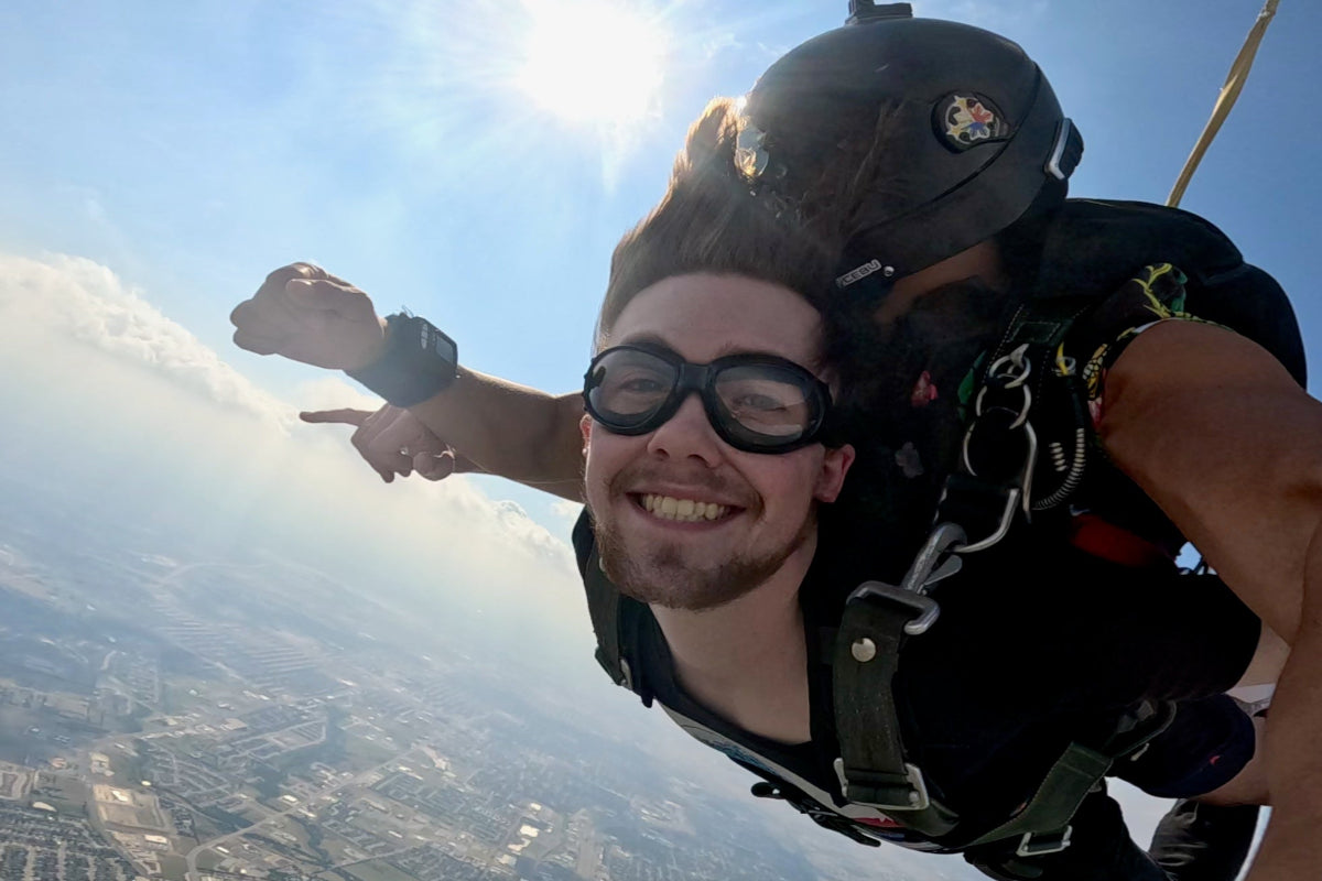 Joyful tandem skydive with a smiling male passenger and instructor in mid-air.