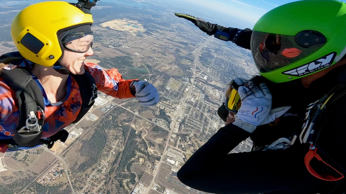 Tandem skydivers smiling in freefall with an outside videographer capturing the moment.