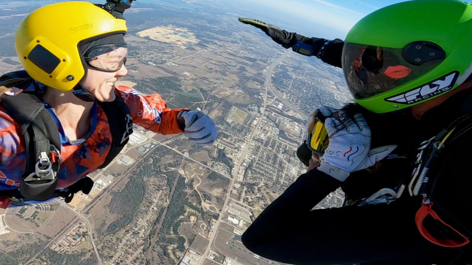 Tandem skydivers smiling in freefall with an outside videographer capturing the moment.